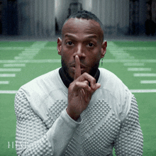 a man in a white sweater is making a shhh gesture