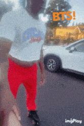 a man in a crop top and red pants is standing in front of a white car that says bts on it