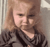 a little girl is making a funny face while looking out of a window .