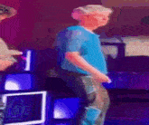 a man in a blue shirt is dancing in a room with purple lights