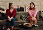 two women sit on a couch with a bowl of food and a bottle with the letter r on it