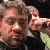 a man is singing into a microphone while another man looks on .
