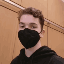 a young man wearing a black face mask is looking at the camera