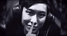 a black and white photo of a woman wearing headphones holding her finger to her mouth .
