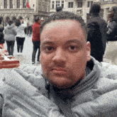 a man in a grey jacket looks at the camera with a crowd in the background