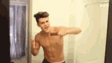 a shirtless young man is brushing his teeth in front of a mirror .