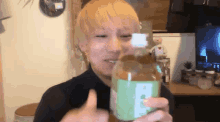 a man with blonde hair is holding a bottle and giving the thumbs up sign