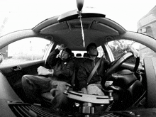 a black and white photo of two men sitting in a car with a umbrella hanging from the ceiling