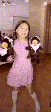 a girl in a pink dress is holding a stuffed animal