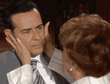 a woman is touching a man 's face in a suit and tie