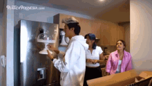 a man is putting a cake stand on a refrigerator door while two women look on ..