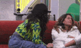 two women are sitting on a red couch holding hands and talking .
