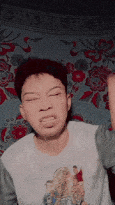 a young boy making a funny face in front of a floral blanket