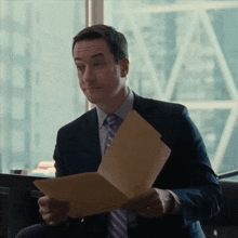 a man in a suit and tie is holding a folder of paper