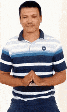 a man wearing a blue and white striped shirt has his eyes closed and his hands folded