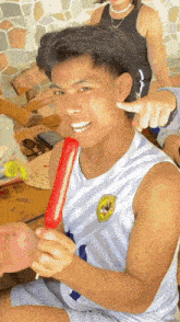 a young man is eating a red popsicle with a mickey mouse patch on his jersey