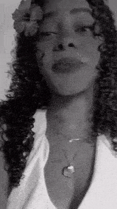 a woman with curly hair and a flower in her hair is wearing a necklace .
