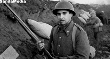 a man in a military uniform is holding a rifle in front of a sand media logo