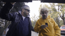 a man in a yellow hoodie is holding a cell phone