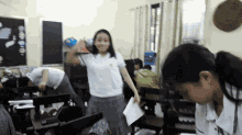 a girl in a white shirt with the letter a on it is standing in a classroom