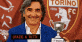 a man is holding a trophy in front of a torino fc logo