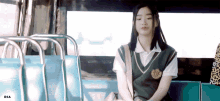 a girl in a school uniform is sitting on a bus with the word dia below her