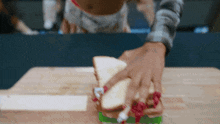 a close up of a person making a sandwich on a wooden cutting board
