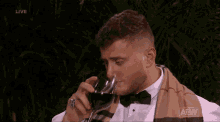 a man in a tuxedo is drinking a glass of wine with the aew logo in the corner