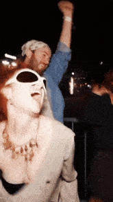 a woman wearing sunglasses is dancing with a man in a bandana behind her