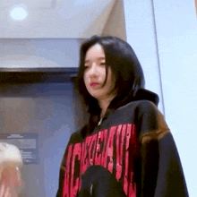 a woman wearing a red and black hoodie is standing in front of an elevator .