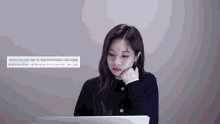 a woman sitting in front of a laptop with a foreign language written on the bottom