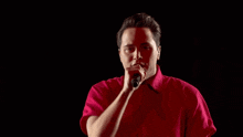 a young man in a red shirt is singing into a microphone