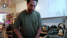 a man in a green shirt is washing dishes in a kitchen with the letters h- above him