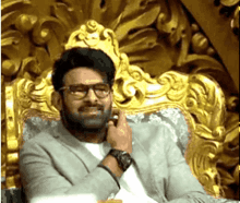 a man in a suit and glasses is sitting in a gold chair