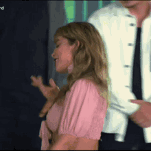 a woman in a pink top is dancing with a man in a white jacket behind her