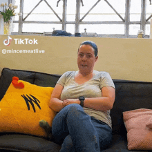 a woman sitting on a couch with a yellow pillow that says ' chicken ' on it