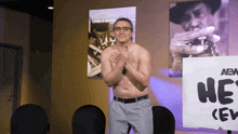 a shirtless man stands in front of a sign that says he 's