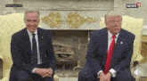 two men in suits and ties are sitting in front of a fireplace with washington dc written on the bottom left