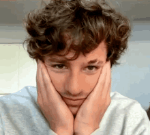 a man with curly hair is making a face with his hands on his face .