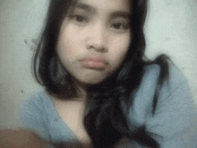 a woman with long black hair and a blue shirt looks at the camera