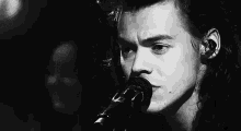 harry styles is singing into a microphone on stage in a black and white photo .
