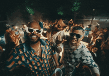 two men wearing sunglasses are standing next to each other in a crowded room
