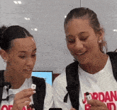 two girls wearing jordan shirts are looking at something