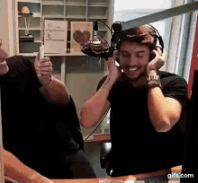 a man wearing headphones is taking a selfie in front of a microphone in a radio studio .