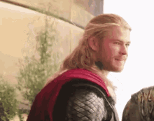 a man with long blonde hair and a beard is wearing a red cape and a leather jacket .