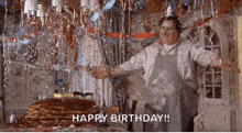 a man in an apron is standing in front of a table with a cake and confetti .