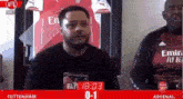a man with a beard is sitting in front of a scoreboard that says tottenham 0-1 arsenal .