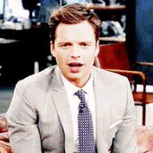 a man in a suit and tie is sitting on a chair with his mouth open