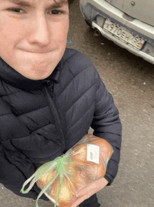 a man holding a bag of bread in front of a car with a license plate that says x910eh-153