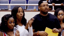 a group of people are sitting in a stadium watching a game and one of them is holding a yellow piece of paper .